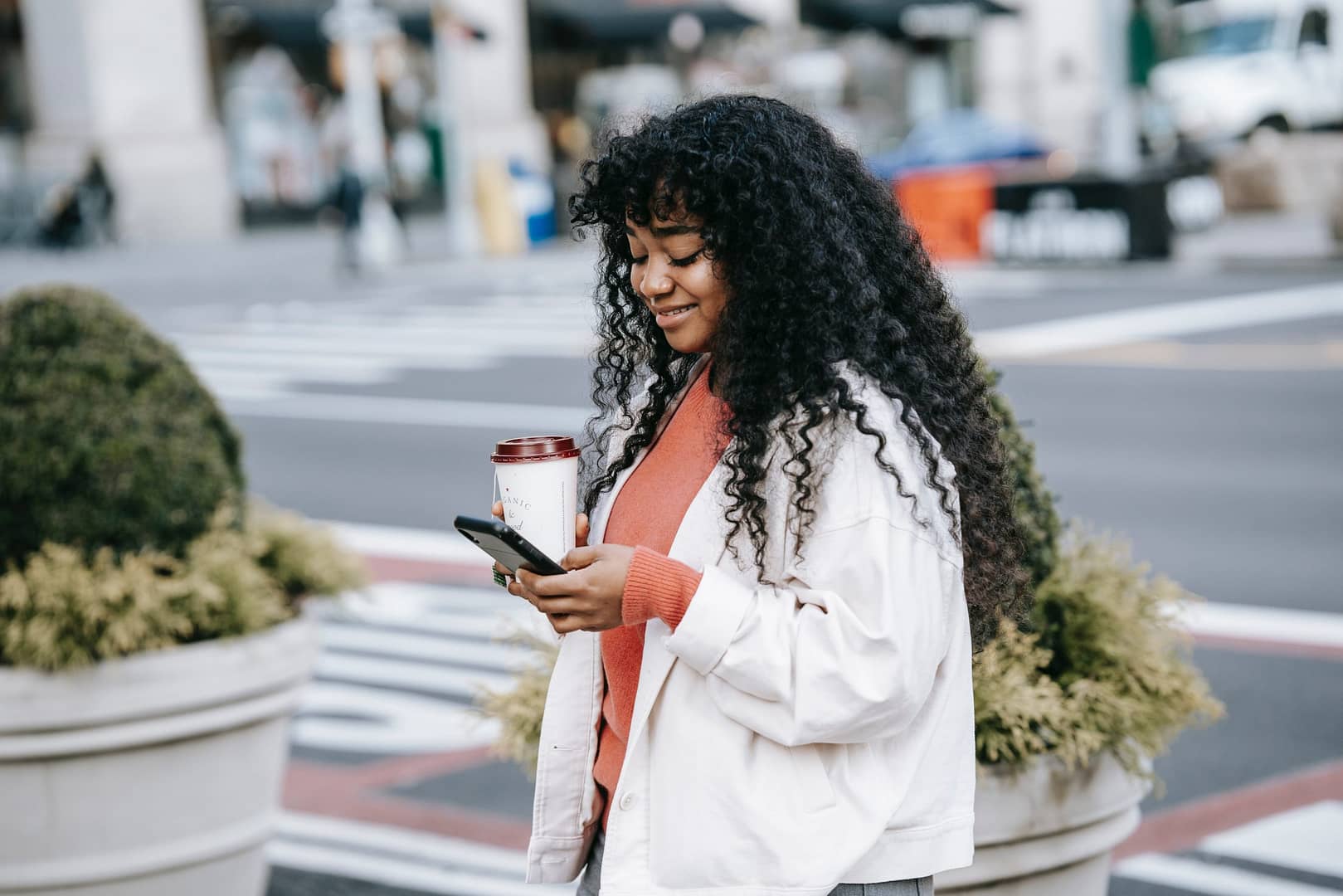Girl walking on road holding a coffee and mobile phone looking at church mobile app